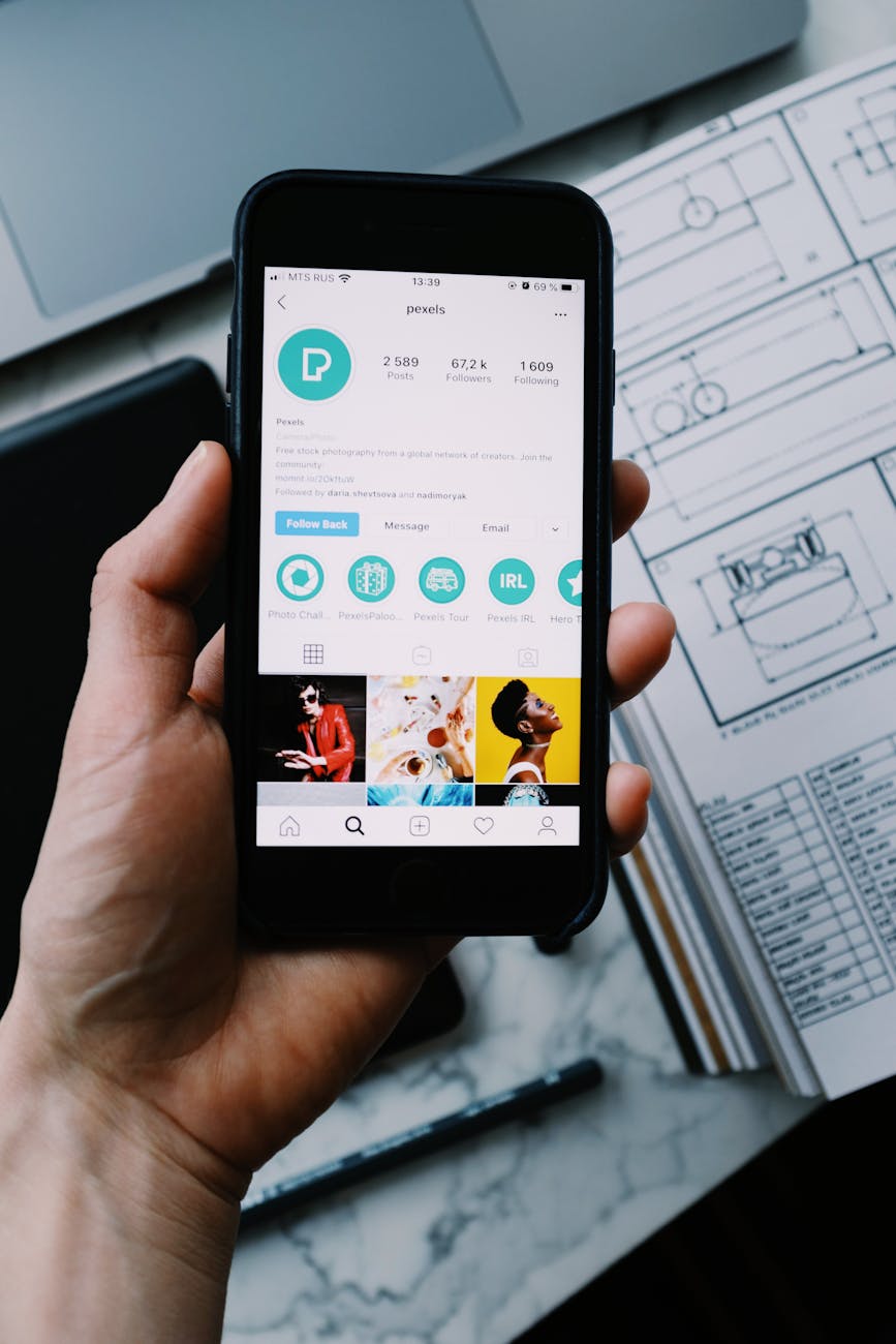 Close-up shot of a hand holding a smartphone with social media app open, on a desk with paperwork.