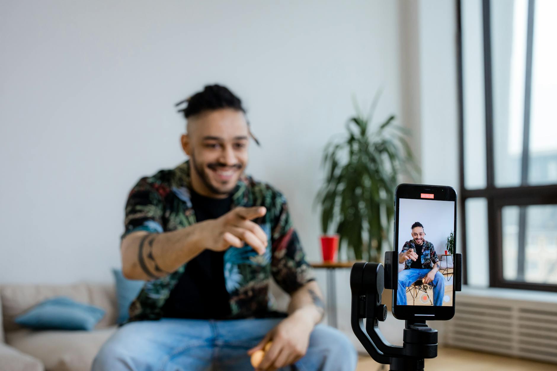 Smiling man recording a video using a smartphone on a gimbal in a bright room.