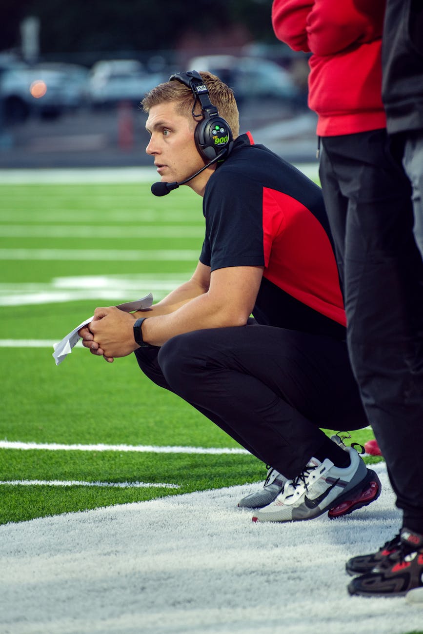 Intense football coach strategizes during a game on the field sidelines.